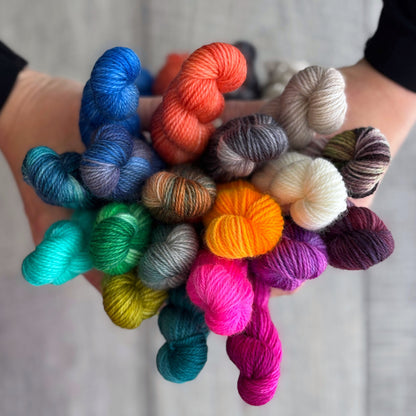 Colourful mini skeins of yarn held in hands against a neutral background