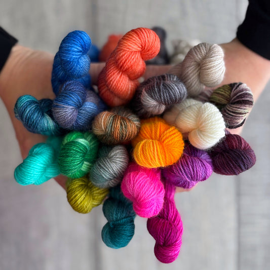 Colourful mini skeins of yarn held in hands against a neutral background